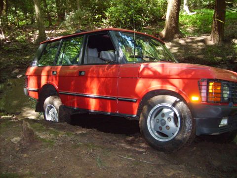 1995 Ford Bronco - A red Range Rover navigates a muddy, wooded path.