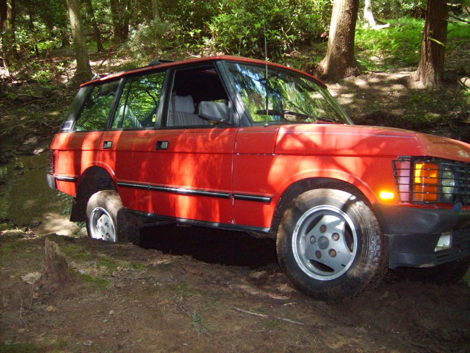 Red Range Rover stuck in mud on a wooded trail
