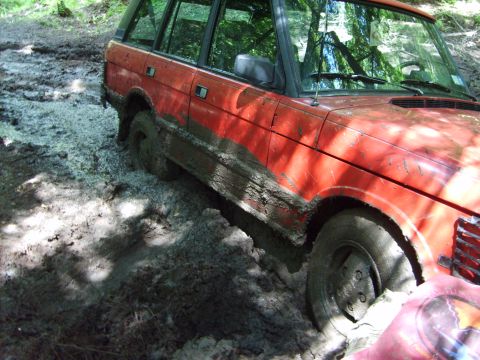 1995 Ford Bronco - This Range Rover is deep in the mud, with trees reflected in the windows.