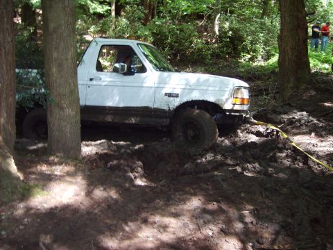 1995 Ford Bronco - A white Ford truck is stuck in the mud off-road, with trees surrounding the scene.