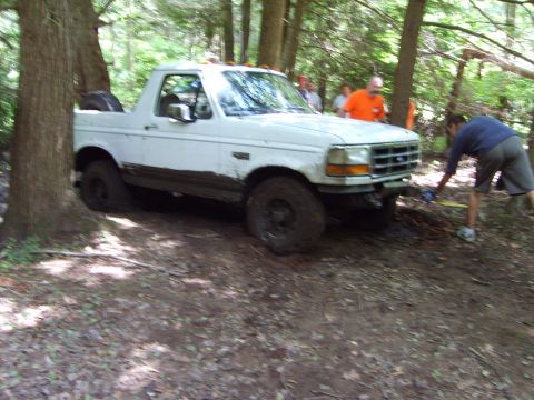 1995 Ford Bronco - A white 1995 Ford Bronco is stuck in the mud off-road, with people nearby.