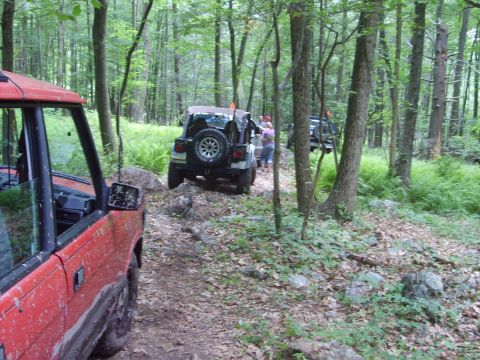 1995 Ford Bronco - Multiple off-road vehicles navigate a rocky path through a dense forest.
