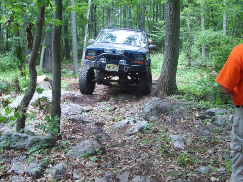 1995 Ford Bronco - A blue Jeep Cherokee XJ navigates a rocky trail in a wooded area.