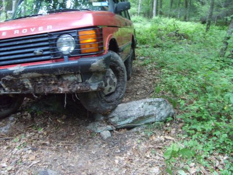 1995 Ford Bronco - This red Range Rover is navigating a rocky trail in a forest setting.