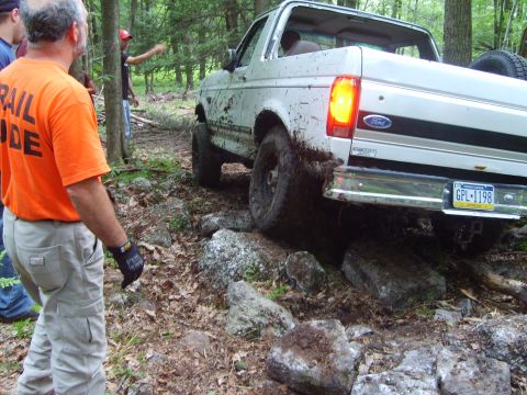 1995 Ford Bronco - White 1995 Ford Bronco tackles a challenging off-road course with mud and rocks.