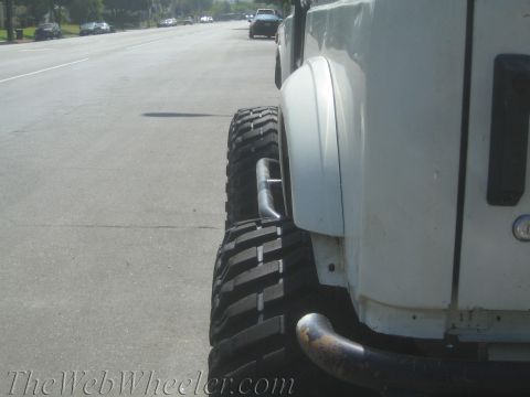 1987 Suzuki Samurai - A white SUV with oversized tires is parked on the side of a road, with other vehicles visible in the distance.