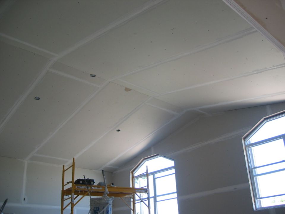 Scaffolding and drywall on a vaulted ceiling under construction, with arched windows