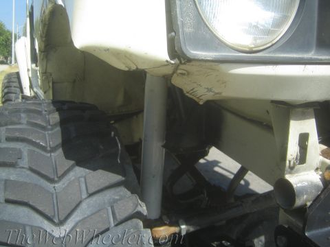 1987 Suzuki Samurai - Close-up of a white 1987 Suzuki Samurai's front section, showing a large off-road tire and damaged fender.
