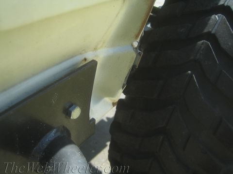 1987 Suzuki Samurai - Detail of a vehicle's body and tire, showing some rust and a bolted bracket.