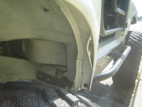 1987 Suzuki Samurai - Close-up view of the frame and roll cage of a modified off-road vehicle, with a large tire visible.