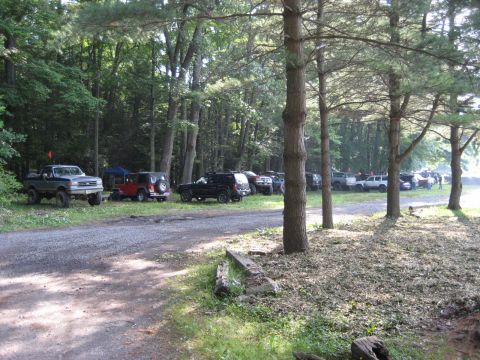 1991 Ford Bronco - Multiple off-road vehicles are parked in a wooded area, likely at an event.