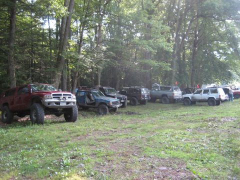 1991 Ford Bronco - A group of modified off-road vehicles are gathered in a wooded area.