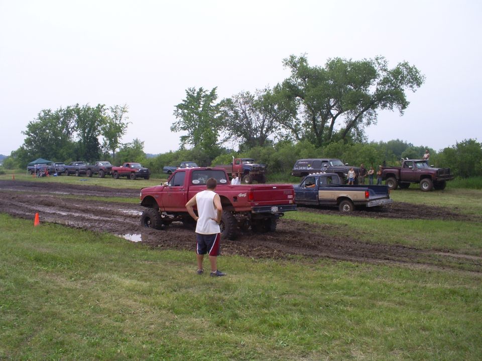 Red pickup truck with large tires in mud, rear view. Mud drags event