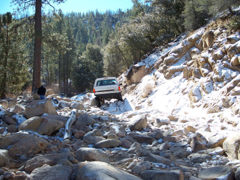 1996 Ford Bronco - White 1996 Ford Bronco navigates a challenging off-road trail with snow and rocks.