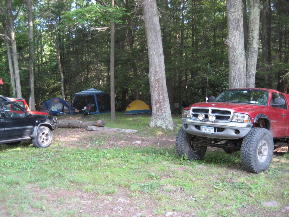 Red pickup truck with large tires parked at a campsite