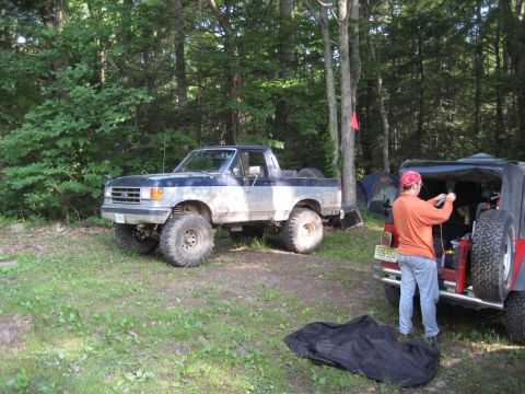 1991 Ford Bronco - Two off-road vehicles are parked at a campsite in a wooded area.