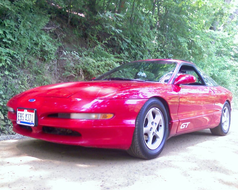 Red 1993 Ford Probe GT parked on a dirt road with trees in the background. License plate EBS 4371 is visible