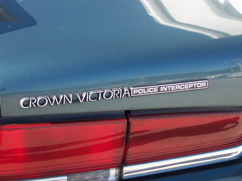 Crown Victoria Police Interceptor badge on a teal car's trunk lid, above a red taillight
