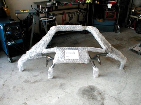 1996 Ford Bronco - A front bumper, wrapped in protective bubble wrap, sits on a concrete floor next to a welding machine.
