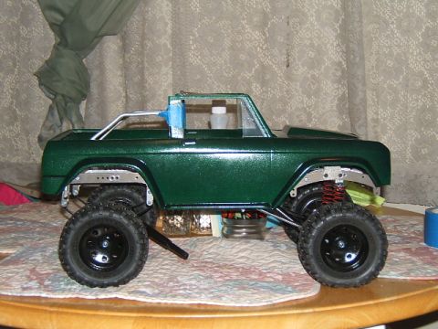 1988 Ford Bronco - A green RC crawler model sits on a patterned cloth, displaying its suspension and off-road tires.