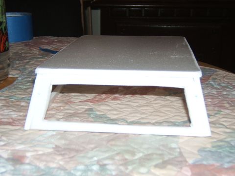 1988 Ford Bronco - A white plastic stand is positioned on a patterned tablecloth, with a roll of blue tape visible in the background.