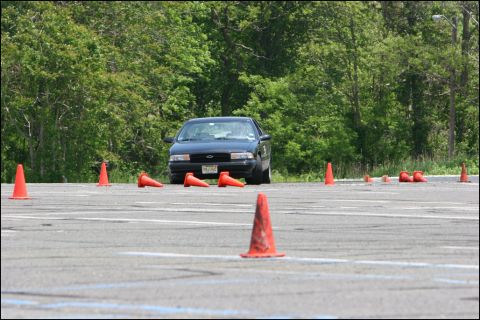 2001 Mercury Grand Marquis - A dark sedan navigates a course marked by orange traffic cones on a paved lot.