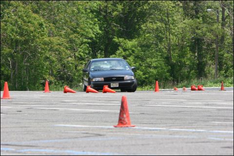 2001 Mercury Grand Marquis - A dark sedan navigates a course marked by orange cones on a sunny day.