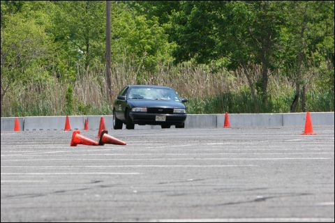 2001 Mercury Grand Marquis - A dark sedan drives through an obstacle course marked by orange cones on a paved lot.