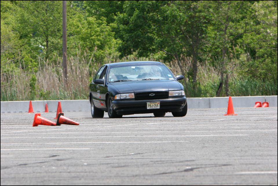 Black sedan navigating an autocross course with orange cones