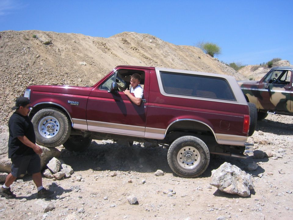 Red 1996 Ford Bronco on a rocky trail, driver visible