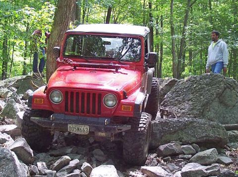 2003 Jeep Wrangler - A red 2003 Jeep Wrangler tackles a challenging rocky off-road course with a person watching.