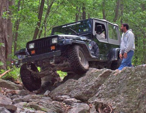 2003 Jeep Wrangler - A black Jeep Wrangler TJ navigates a rocky trail during an off-road event, with a "Jeep Jamboree USA" sticker on the windshield.