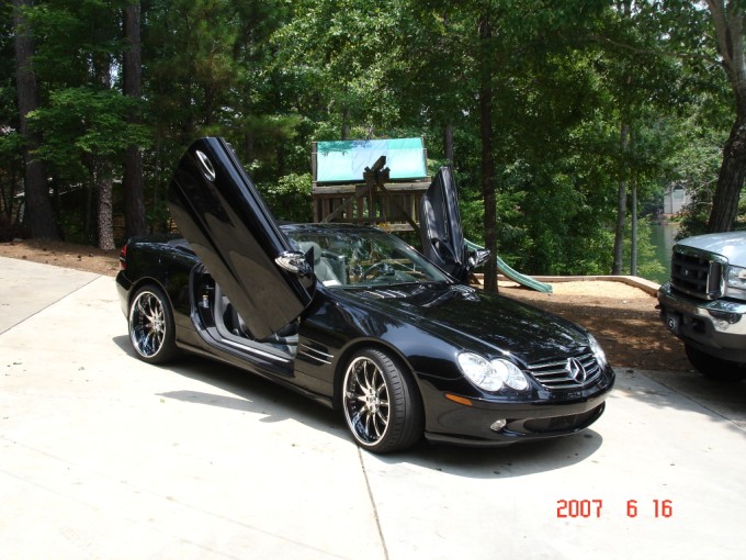 Black Mercedes SL convertible with vertical scissor doors and chrome wheels on a driveway