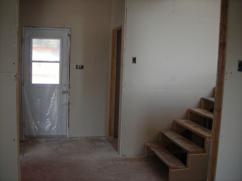 1984 Ford Bronco - Unfinished interior of a house showing drywall, a covered door, and wooden stairs.