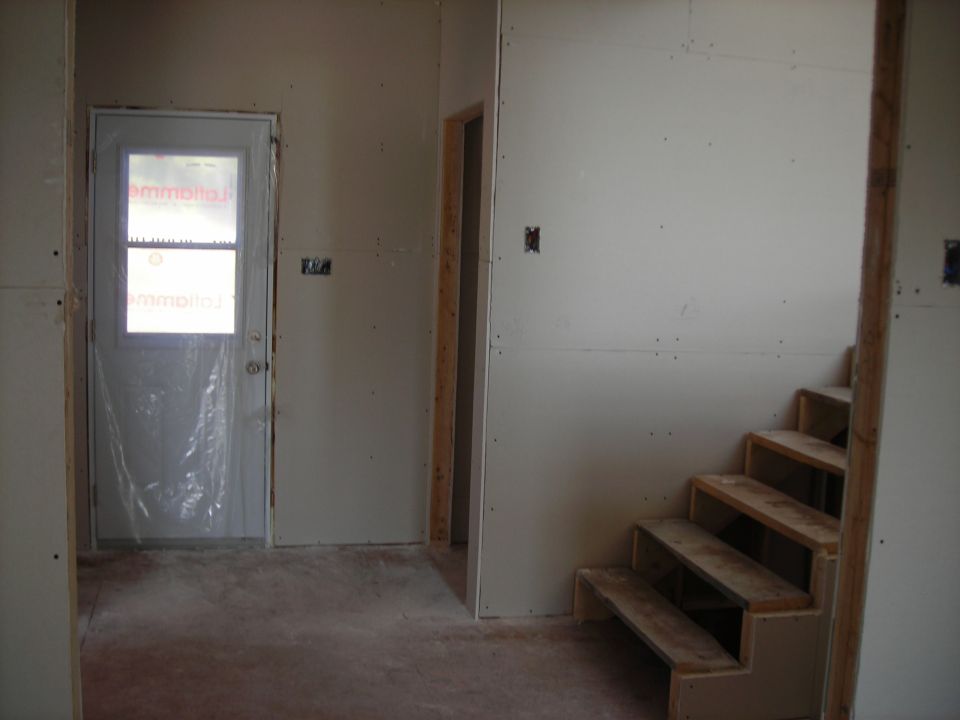 Interior of a house under construction with unfinished walls, a door covered in plastic, and wooden stairs