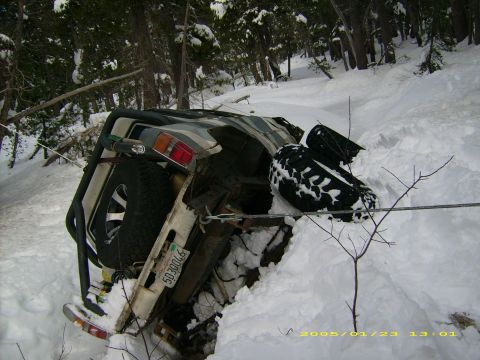 1986 Ford Bronco - An off-road vehicle is overturned in a snowy landscape, with its spare tire visible.