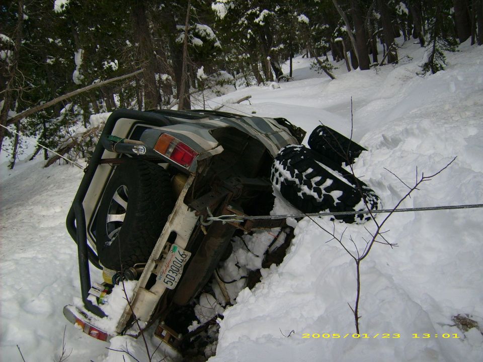 Off-road vehicle on its side in snow, showing a spare tire and a license plate reading 5030046