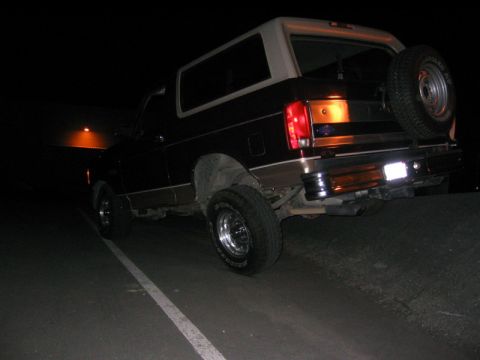 1996 Ford Bronco - The rear of a Ford Bronco is visible at night, parked on a road with a white line.