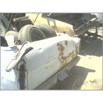 1973 Ford Ranchero - A heavily rusted car trunk sits in a junkyard with other vehicles and tires visible.