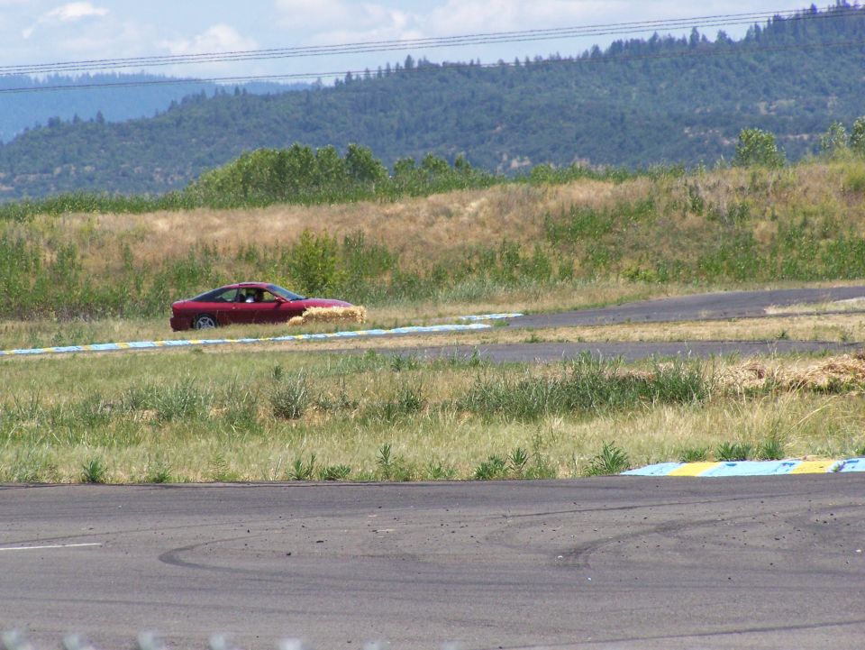 Red coupe with hay bales on its side on a race track
