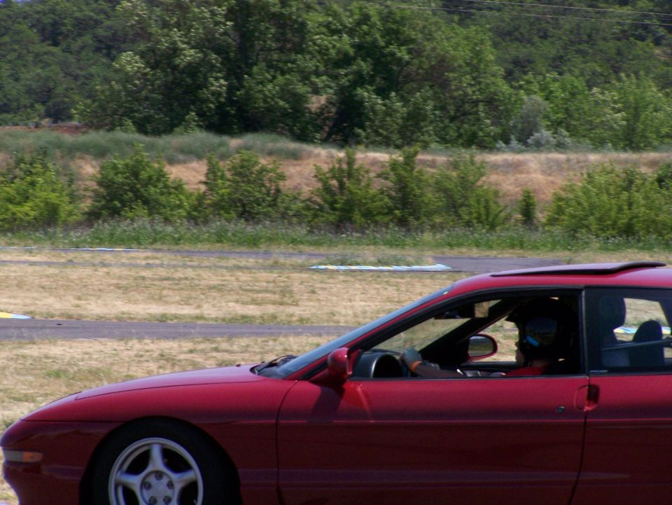 Red coupe with sunroof, driver wearing helmet, side view