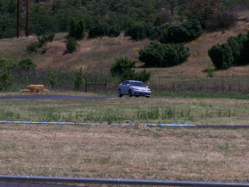 Silver 2007 Mazda 3 sedan driving on a track with grassy hills in background