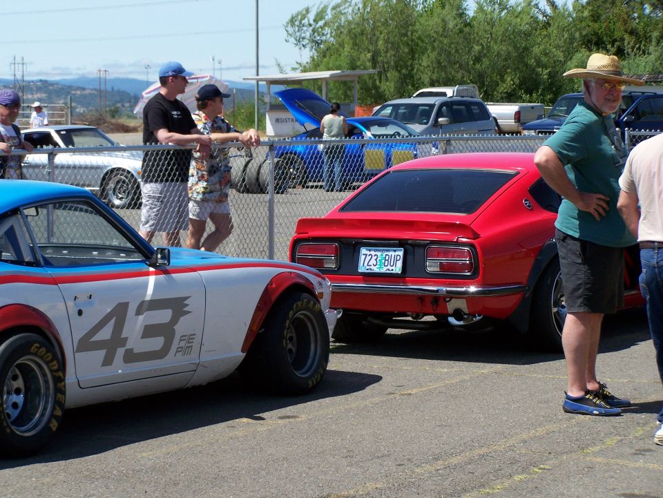 Red sports car with license plate 723 BUP parked next to a white and blue race car