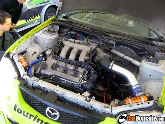 Engine bay of a green Mazda race car with turbocharger piping
