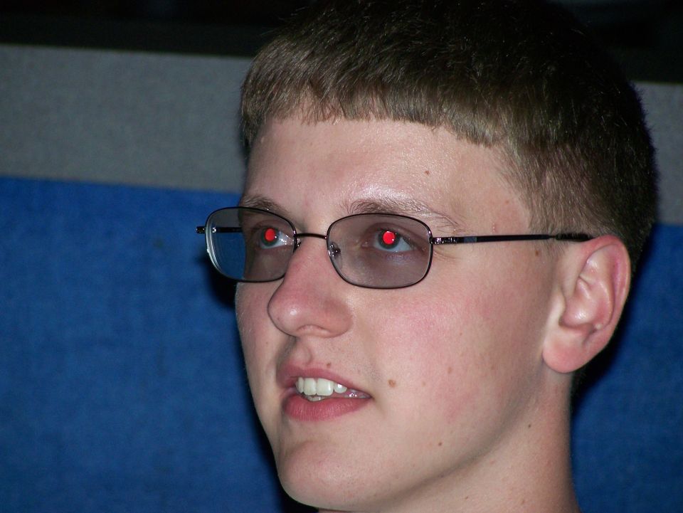Close-up of a young person wearing glasses with red pupils, looking to the side