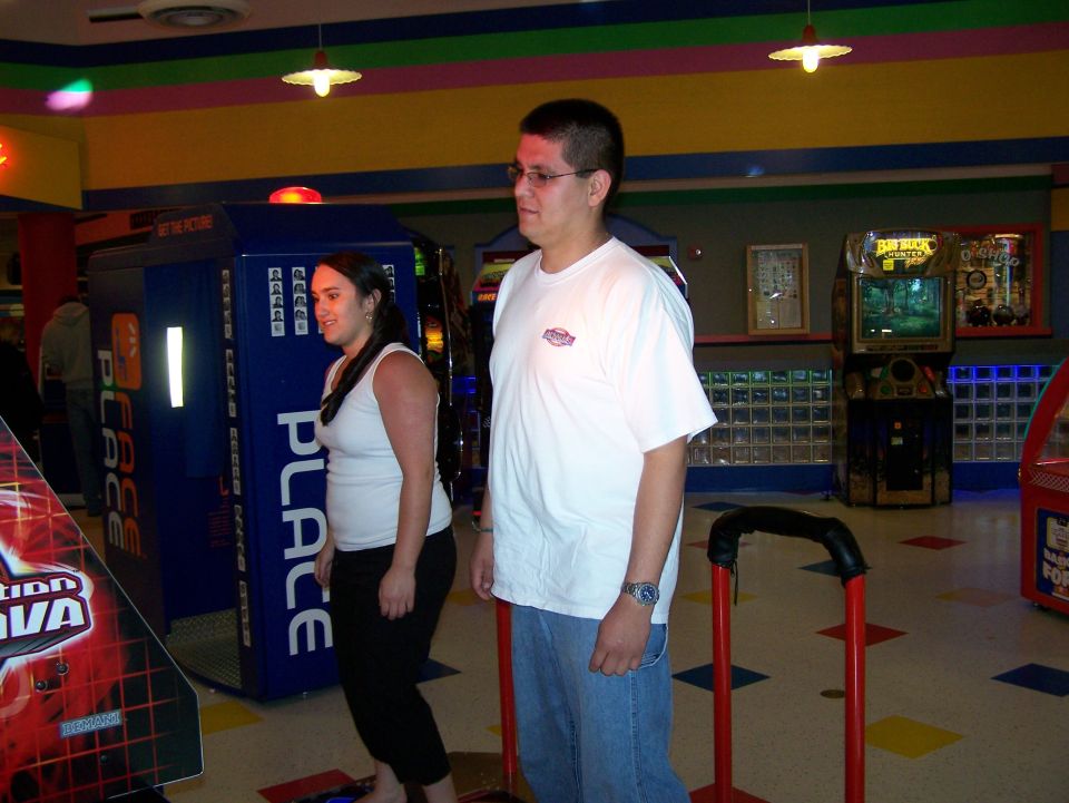 Man and woman stand near arcade machines in a brightly lit entertainment center