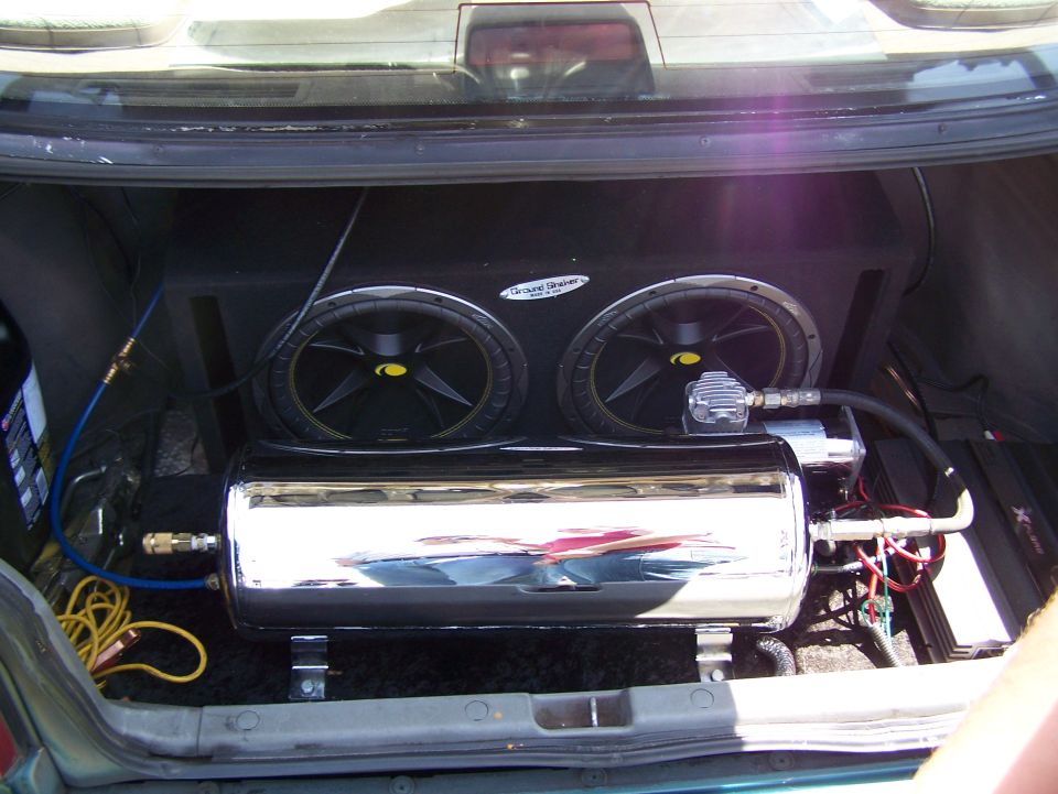 Car trunk with two subwoofers, a chrome air tank, and an amplifier