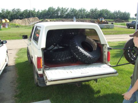 1990 Ford Bronco - The rear of a white Ford Bronco is open, revealing several large spare tires packed inside.