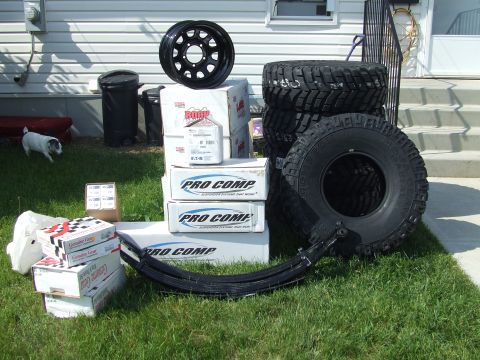 1990 Ford Bronco - New Pro Comp suspension parts and tires are laid out on the lawn, ready for installation.