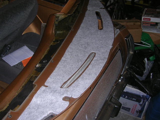 Dashboard panel with gray carpet padding being installed. Some of the original brown trim is visible